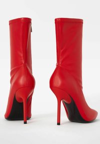 Červené kotníkové boty na vysokém podpatku s hladkým koženým povrchem, zužujícím se tvarem a tenkým stiletto podpatkem. Obsahují boční zip a ševové detaily.
