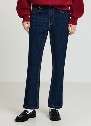 Dunkelblaue Jeans aus Denim mit geradem Schnitt, ausgestattet mit klassischem Fünf-Taschen-Design und kontrastierenden Nähten. Das Modell trägt schwarze Loafers.