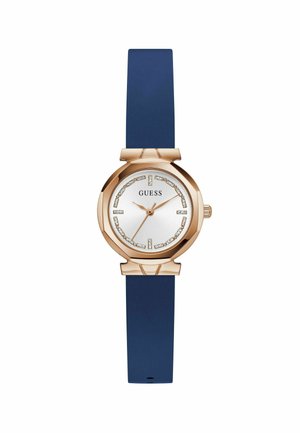 Orologio oro rosa con quadrante accentuato da cristalli e cinturino in silicone blu, con il marchio "GUESS" visibile sul quadrante.