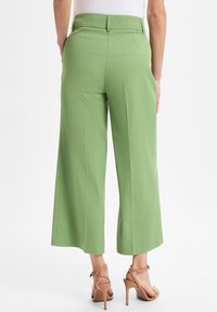 Grüne weit geschnittene Hose aus einem glatten, weichen Material, mit hohem Bund und einem schlichten Finish. Kombiniert mit braunen Sandalen mit hohen, schmalen Trägern.