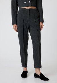 Pantalons gris ajustés en tissu doux, avec une taille plate, deux plis et une coupe slim, associés à des mocassins noirs.