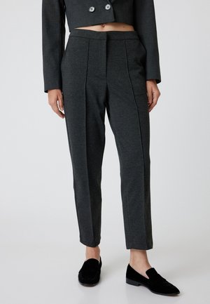 Grijze op maat gemaakte broeken van zachte stof, met een platte voorkant, twee plooien en een slim fit, gecombineerd met zwarte instappers.