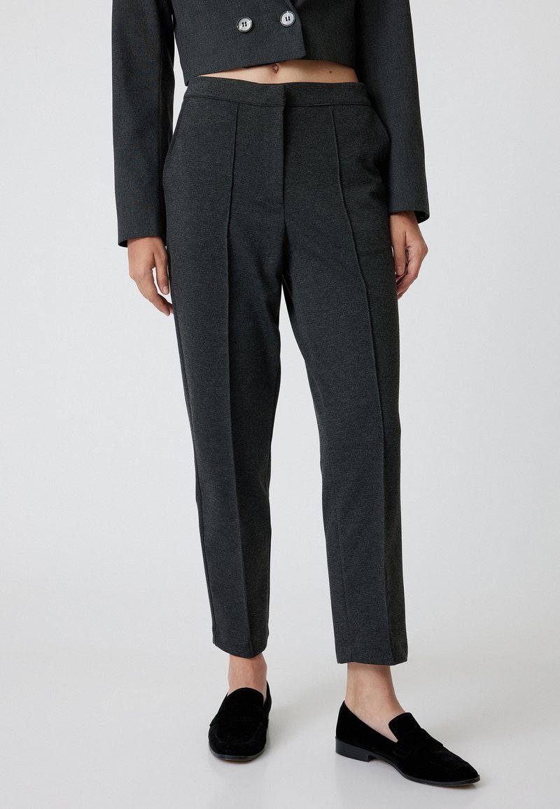 Pantalons gris ajustés en tissu doux, avec une taille plate, deux plis et une coupe slim, associés à des mocassins noirs.