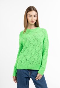 Kötött, lime zöld pulóver geometrikus mintákkal és pompon részletekkel. Kerek nyakkivágással és bordázott ujjak passzolnak hozzá, farmernadrággal párosítva.