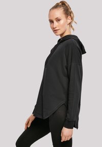 Schwarzer Kapuzenpullover mit lockerer Passform, überschnittenen Schultern und asymmetrischem Saum. Hergestellt aus weichem Material, mit einem Reißverschluss auf der Vorderseite und minimalistischem Design.