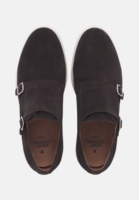 Chaussures en daim marron avec semelles blanches, dotées de deux boucles en argent et d'un design à bout rond. Texture douce et style minimaliste.