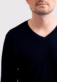 Marinblå v-ringad tröja i fint stickad tyg, med ribbad krage och ärmslut, har en mjuk textur och en minimalistisk design.