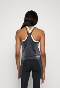 Tmavě šedý sportovní tílko s bílými akcenty, se zadním výstřihem ve stylu racerback a texturovaným materiálem. Zobrazeno zezadu.