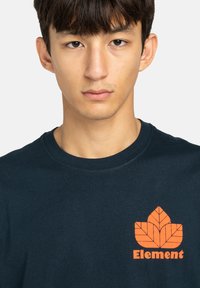 Navy cotton T-shirt featuring an orange leaf design and "Element" text on the front. Round neckline and short sleeves. Smooth texture.