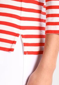 Rot-weiße gestreifte Baumwollbluse mit Dreiviertelärmeln und seitlichen Schlitzen am Saum. Weicher Stoff und lässiges Design.