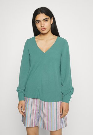 Top de mangas longas na cor turquesa com decote em V e detalhes de mangas franzidas, combinado com calções listrados multicoloridos. Tecido macio e leve.