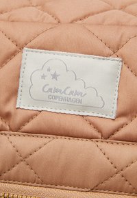 Tissu matelassé de couleur pêche douce, avec une étiquette blanche ornée d'un design de nuage et "Cam Cam COPENHAGEN" en texte gris. Détails de couture visibles.