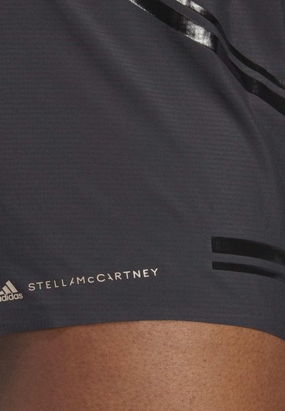 Pantaloni sportivi neri con un motivo testurizzato, caratterizzati da strisce nere lucide e un logo dorato "STELLAMcCARTNEY" sul lato.
