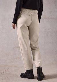 Beige tapsweatpants met een zachte textuur, voorzien van een hoge tailleband, achterzakken en gecombineerd met zwarte enkellaarsjes.