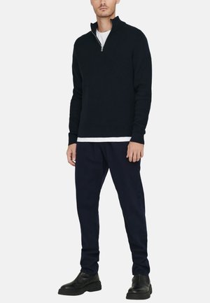 Navy knitted pullover with a half-zip collar, worn over a white t-shirt. Paired with dark pants and black leather ankle boots.