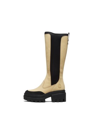 Botte haute en cuir beige et noir avec semelle et talon noirs épais, avec une languette à l'arrière et des détails sur le panneau latéral.