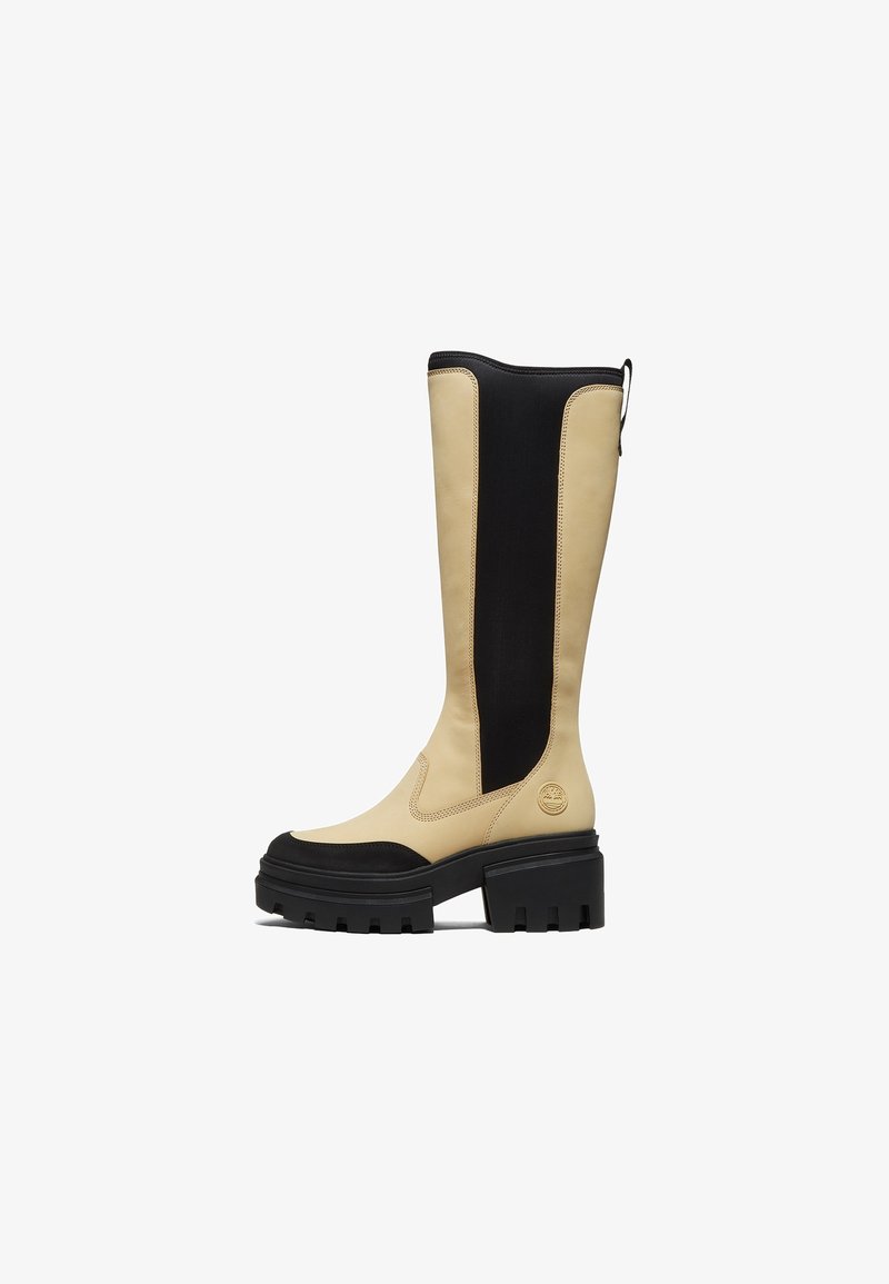 Botte haute en cuir beige et noir avec semelle et talon noirs épais, avec une languette à l'arrière et des détails sur le panneau latéral.