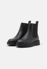Černé kožené Chelsea boty s elastickými bočními panely a poutky, s plochou podrážkou a minimalistickým designem. Hladký povrch a elegantní tvar.