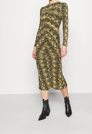 Langselt, aansluitend jurkje met een zwart-gele abstracte print. De stof is gestructureerd; het reikt tot halverwege de kuit. Draag het met zwarte enkellaarsjes.