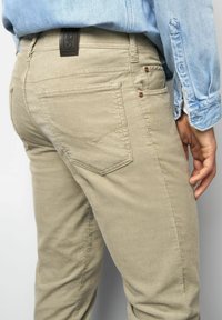 Beige corduroy pants worn by a person with a light blue denim shirt tucked in, showing back pocket and hand relaxed by side.