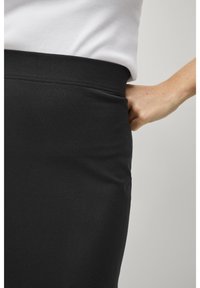 Schwarzer, elastischer Rock mit glatter Textur und elastischem Bund. Nahaufnahme von der Seite, die das figurbetonte Design und die elegante Silhouette zeigt.