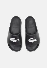 Sandale negre tip flip-flop cu o talpă texturată, design cu vârful deschis și un logo alb de crocodil pe partea superioară. Realizate din material sintetic durabil.