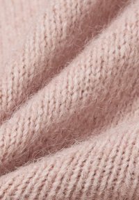 Hellrosa gestrickter Stoff mit einer weichen, flauschigen Textur und einem Rippenmuster, das feine Garn-Details und eine leicht lockere Webart zeigt.