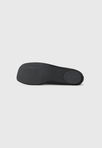 Semelle de chaussure noire avec un design lisse et plat. Présente des motifs de grip texturés et une zone de orteil arrondie pour une meilleure stabilité.