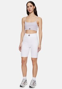 Lila ribbad crop top med tunna band, matchad med vita åtsittande cykelbyxor som har ett logomärke på midjan. Silverfärgade träningsskor.