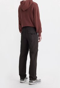 Bordový kapucňový svetr s uvolněným střihem, spárovaný s černými cargo kalhotami s kapsami a stahovacími šňůrkami v pase. Šedé sportovní boty.