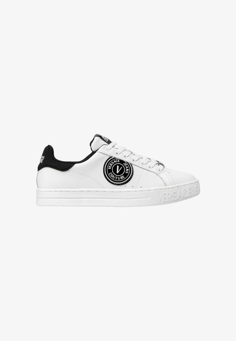 Baskets blanches avec une finition en cuir lisse, accents noirs au talon et au col, dotées d'un patch de logo rond et de branding moulé sur la semelle.
