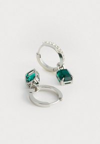 Sudraba apli auskari ar smaragda zaļiem dārgakmeņiem. Iekļauj strukturētu dizainu un mazus caurspīdīgus rhinestone akcentus aplī.
