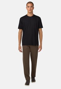 Juoda trumpomis rankovėmis marškinėliai derinami su rudais kelnėmis ir tamsiais avalynė, pasižymintys paprastu dizainu ir glotnia tekstūra.