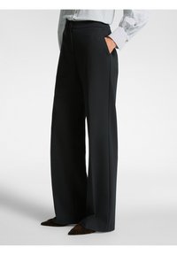 Zwarte wijde pantalon van een soepele stof, met een hoge taille en zijzakken. Gecombineerd met een gestreepte blouse en puntige schoenen.