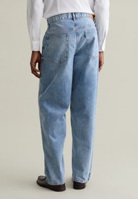 Vaqueros de mezclilla azul claro con corte holgado, con una cintura de altura media, dos bolsillos traseros y costuras visibles. Combinados con zapatos oscuros.