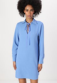 Abito camicia blu con maniche lunghe, colletto e dettaglio con cravatta al collo. Tessuto morbido con una vestibilità relaxed e orlo dritto.