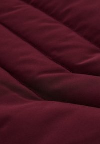 Bordo kvačana tkanina s glatkom teksturom, složenim dizajnom i vidljivim šavnim uzorcima po materijalu.