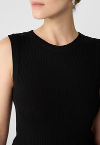 Top senza maniche nero a coste con scollo rotondo, caratterizzato da un tessuto testurizzato e un design aderente. Stile minimalista e contemporaneo.