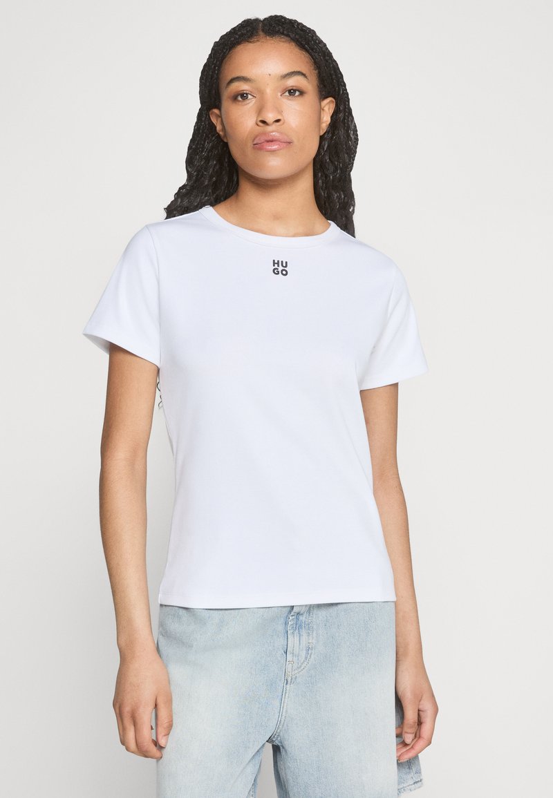 T-shirt bianca in cotone con maniche corte, scollatura rotonda e un piccolo logo nero "HUGO" sulla parte superiore sinistra del petto. Abbinata a pantaloni corti in denim azzurro chiaro.