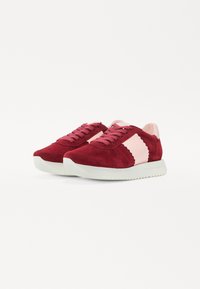 Baskets en suède rouge avec des accents en cuir rose, dessus texturé, lacets plats et une semelle en caoutchouc blanc avec un bord dentelé.