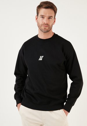Zwarte sweatshirt met lange mouwen, ronde hals en een klein wit logo op de borst. Gemaakt van zachte stof met een relaxte pasvorm.