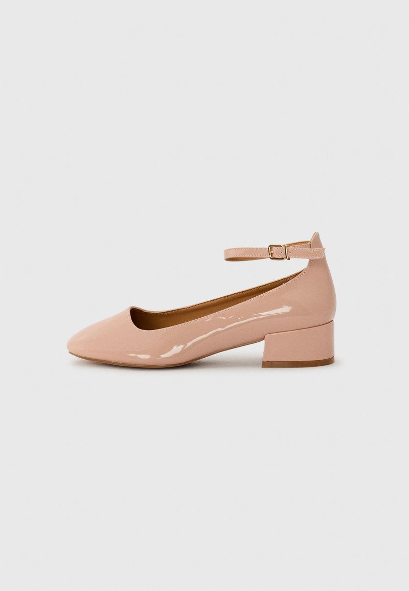 Patent leather pink flat shoe with a rounded toe, ankle strap, and a low block heel. Smooth texture and minimalist design.