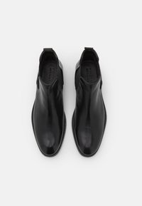 Botas de tobillo de cuero negro con un acabado suave, paneles laterales elásticos, tiradores, punta redonda y costuras detalladas a lo largo de la suela.