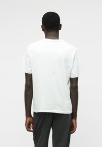 Camiseta blanca de algodón con cuello redondo y mangas cortas, mostrada desde atrás. Textura suave y corte holgado.