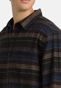 Geruite flanellen shirt met donkere blauwe, zwarte en rode strepen. Bevat een knoopsluiting bij de kraag en een borstzak met een klein logo. Zachte textuur.