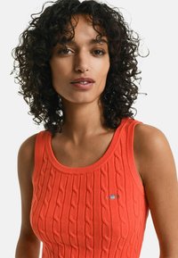 Rode gebreide tanktop met een gestructureerd kabelontwerp, ronde halslijn en een klein geborduurd logo op de borst.