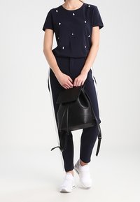 Námořnické tričko s malými bílými dekoračními prvky, spárované s námořnickými kalhotami se bílými bočními pruhy a černým batůžkem na šňůrku.