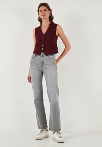 Bordový bezrukávový sveter s predným gombíkom, kombinovaný s svetlošedými rovnými džínami a bielymi teniskami. Hladká tkanina, čistý dizajn.