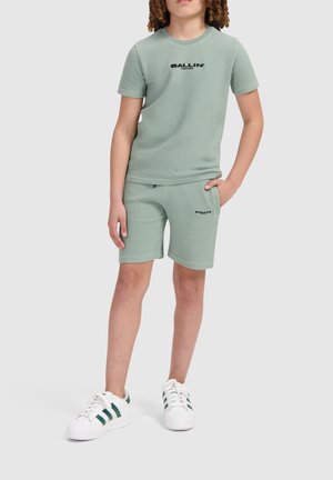Lichtgroene geribde katoenen t-shirt en shorts set met zwarte "BALLIN'" branding. Gecombineerd met witte schoenen met groene strepen.