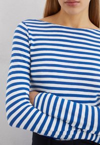 Long-sleeved striped shirt in blue and white, featuring a boat neckline and a soft, stretch cotton fabric. Stripes are evenly spaced.
